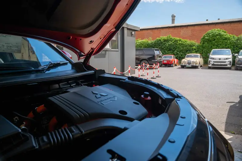 A hybrid engine bay in the My Car Import yard, with a classic Jaguar and a Lancia parked behind